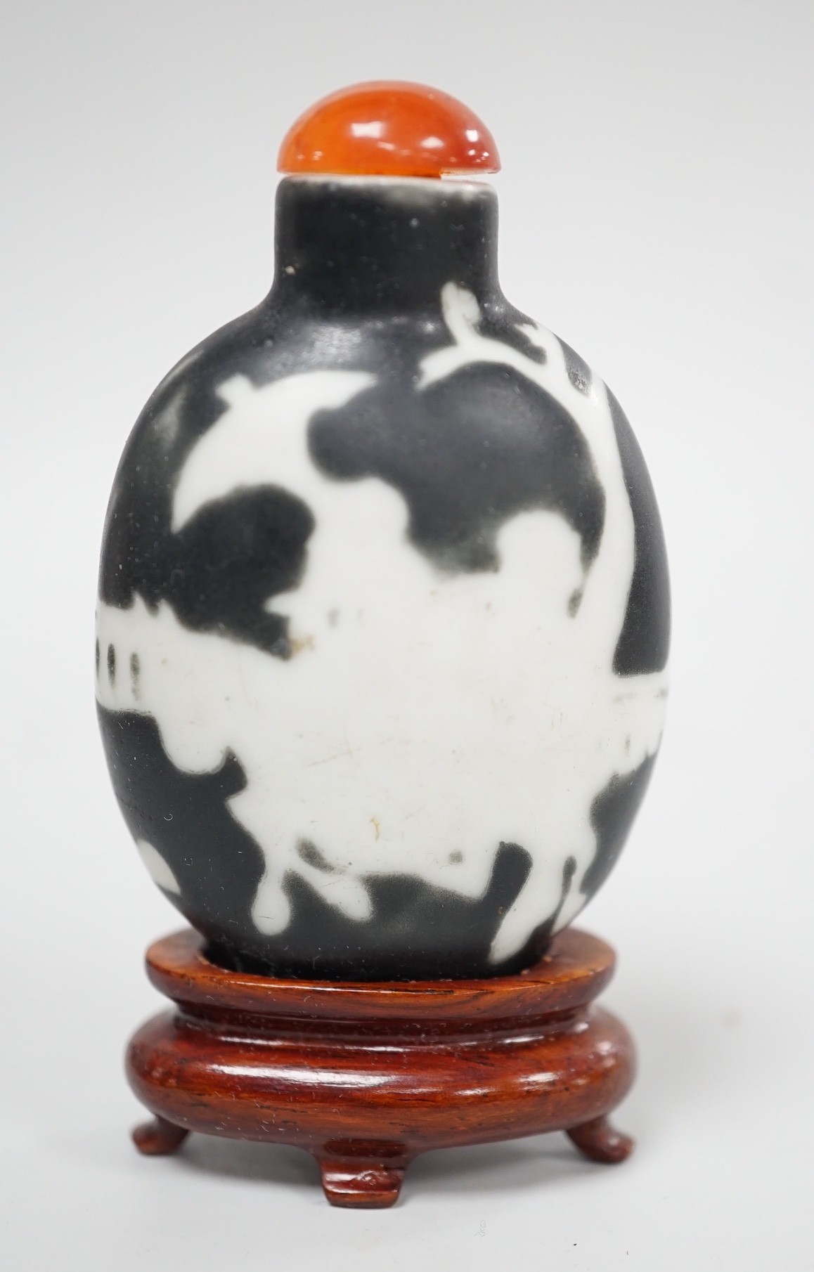 A Chinese porcelain white on black ground silhouette snuff bottle, 5.6 cm excluding stopper and wood stand